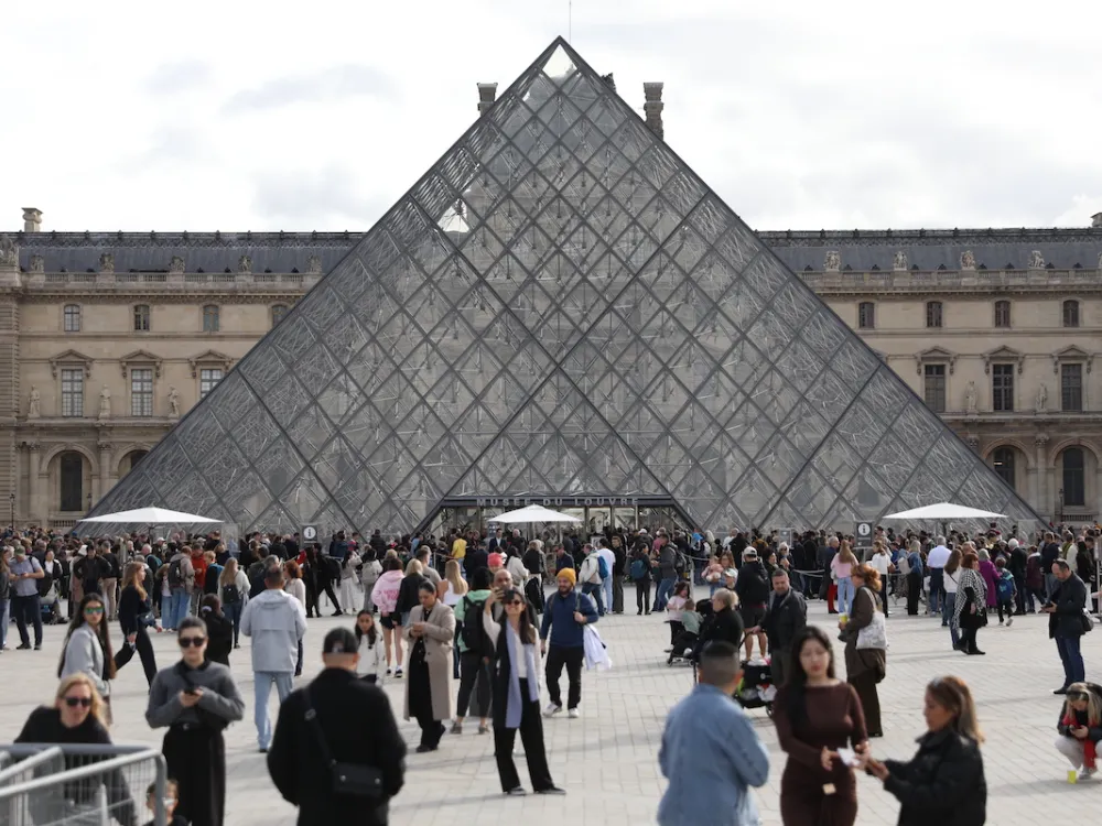 A crowd of people before a glass pyramid.
