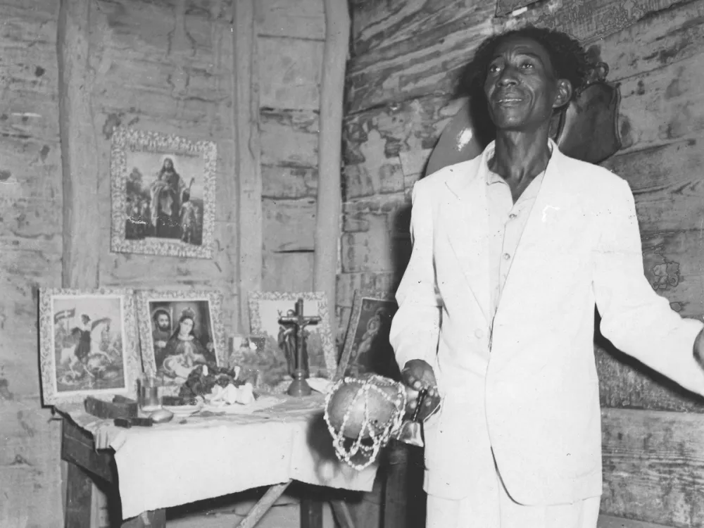A man holding an instrument in front of votive paintings.