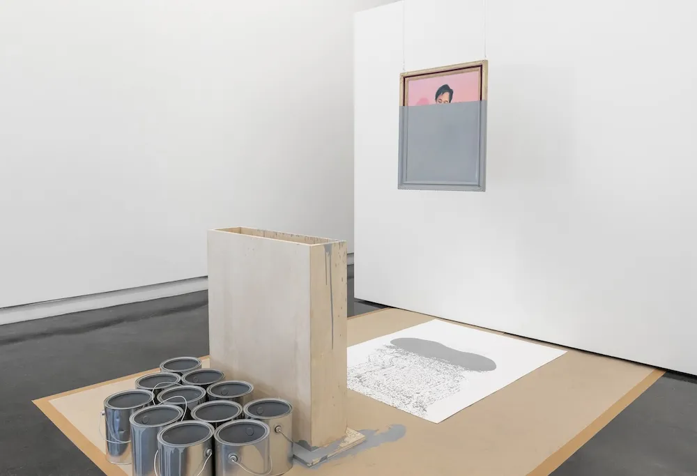 A portrait with a pink background hangs from the ceiling, two thirds of it is covered in grey paint obscuring the subject.