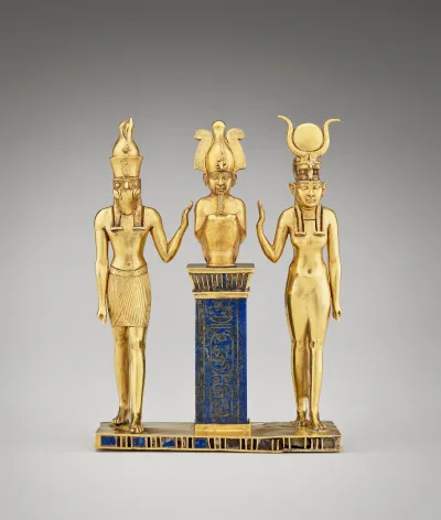 A golden statue of two gods holding one arm each to a central figure with a headdress. The central figure sits on a blue column.