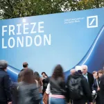 Fairgoers walk in front of a sign for Frieze London.