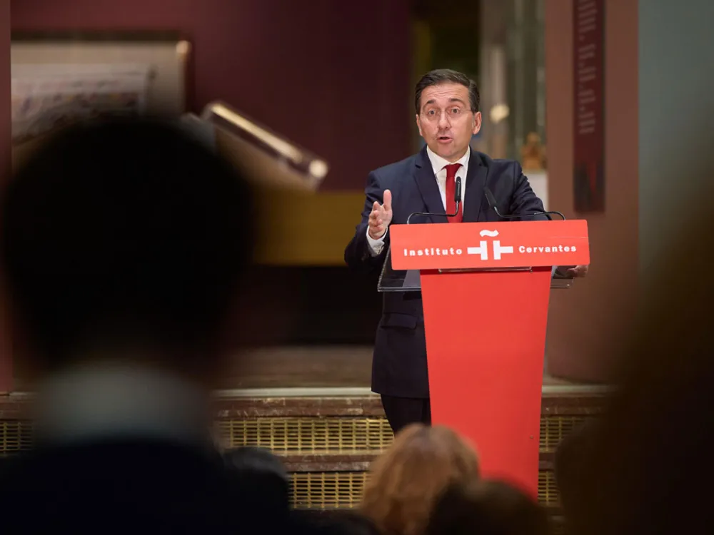 José Manuel Albares speaks at a red podium during a press conference.