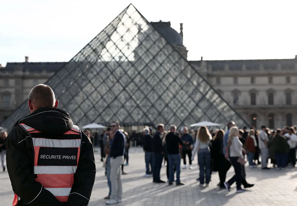 A security guard stands in front of the Pyramide du Louvre, designed by Chinese-US architect Ieoh Ming Pei, with the Louvre Museum in the background in Paris on October 22, 2025. The Louvre Museum reopened its doors to visitors on October 22, 2025 morning for the first time since October 19, 2025