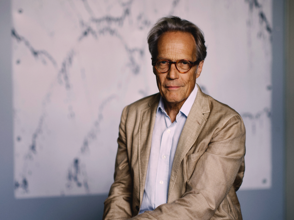 A man in glasses and a tan jacket smiles at the camera.