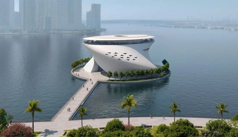 A rendering of a cylindric museum building with a curve going from the upper left to the upper right on a floating island in a body of water.