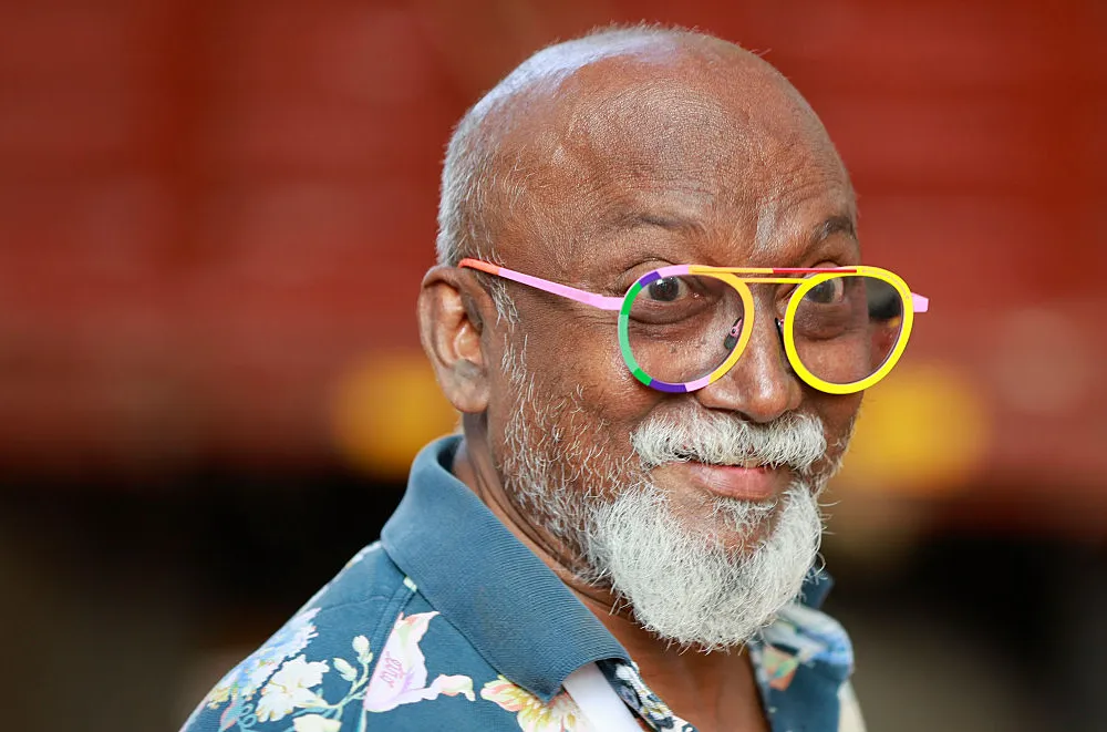 close up of a bald man with a white beard and mustache and colorful eyeglass frames