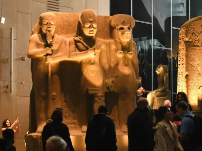 Visitors look at a monumental sculpture of a pharaoh flanked by two ancient Egyptian gods.