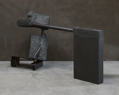 An installation of several black-painted elements, facing a black wall. 