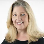 A blond white woman, Mary Anne Carter, smiles for the camera against a blank white background.