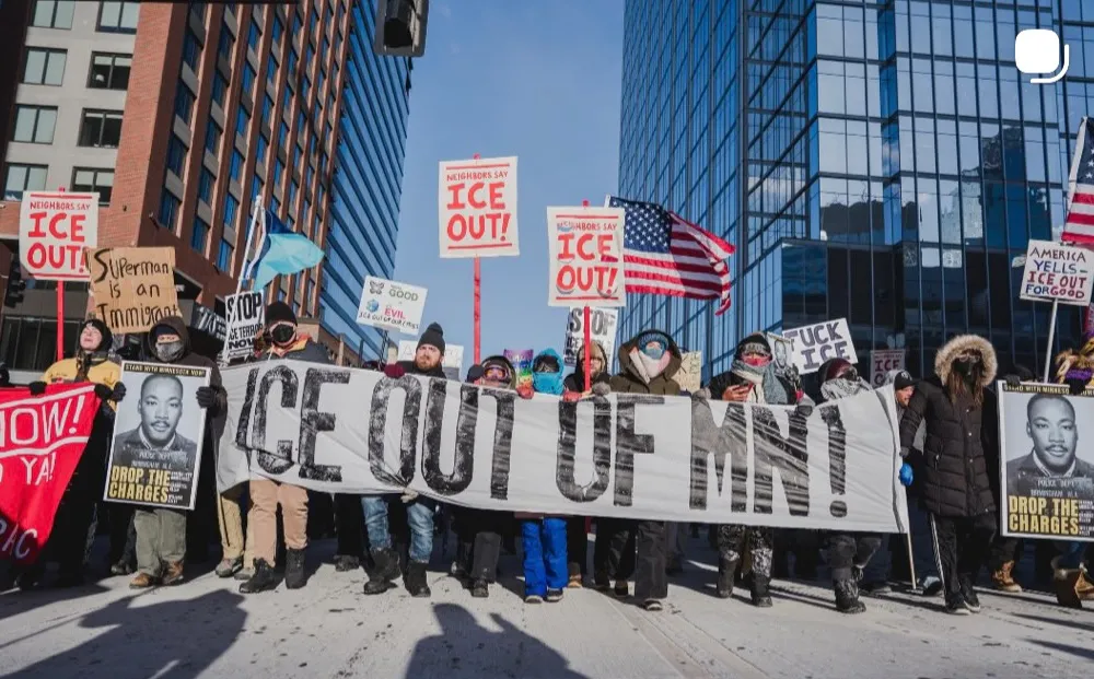 Protesters in Minneapolis carry a banner printed with the words ICE out of MN! and other signs reading 