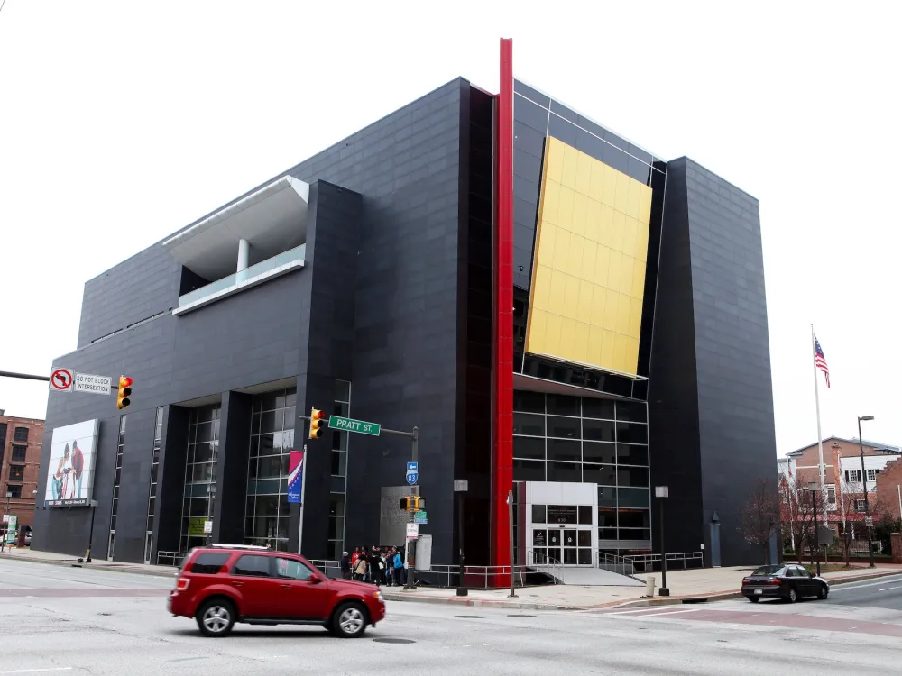 A photo shows the Reginald F. Lewis Museum of Maryland African American History in Baltimore, Maryland. Its architecture is boxy and modernist, with much of the two facades black, with bold geometrical accents in red and yellow.