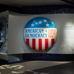 A museum display with a large button reading