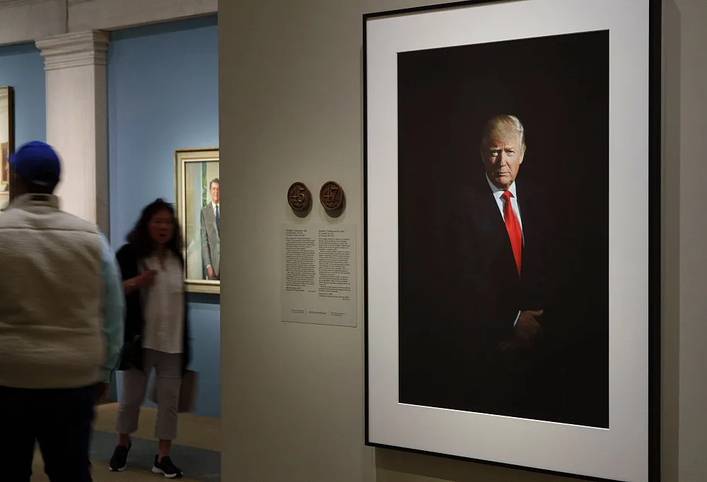 A photograph of a seated man in a red tie on a wall with text next to it.