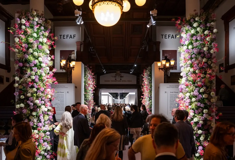 Crowds walk between flower covered columns at TEFAF New York.