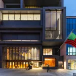 The exterior of museum building that is made of different rectangles of glass and concrete with a US flag in red, green, and black installed out front.