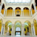 A grand two-story atrium is filled with classical Greco-Roman columns and statues.