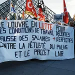 A group of protesters holding a sign in front of a glass pyramid.