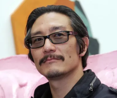 Korean-American artist Michael Joo is photographed at an art exhibition. He wears a black winter jacket and sunglasses.