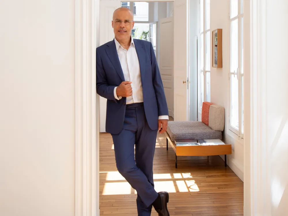 A man, art dealer Kamel Mennour, wears a suit and stands in a sunny art gallery.