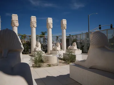 Several sphinxes facing a series of columns with heads at their tops.