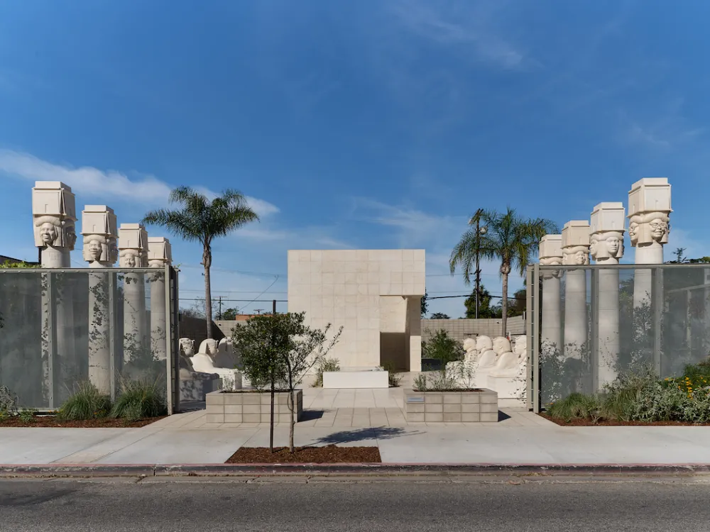 A sculpture park featuring columns with heads at their tops and rows of sphinxes. The park abuts a city street.