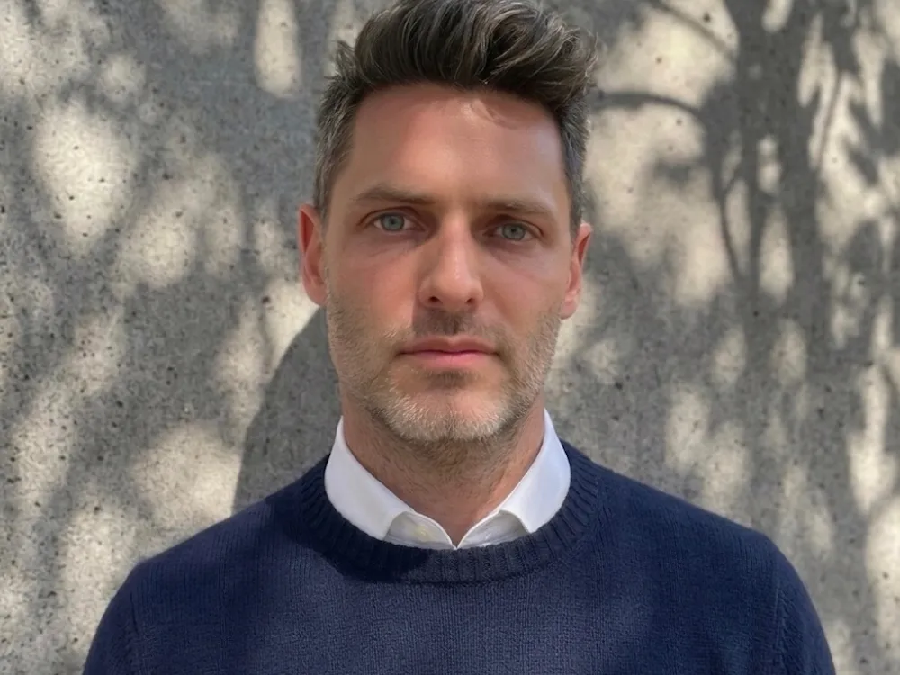 A handsome, strong chinned man in a white shirt and a blue sweater.