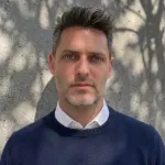 A handsome, strong chinned man in a white shirt and a blue sweater.