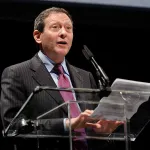 A man at a podium reading from a sheet of paper.