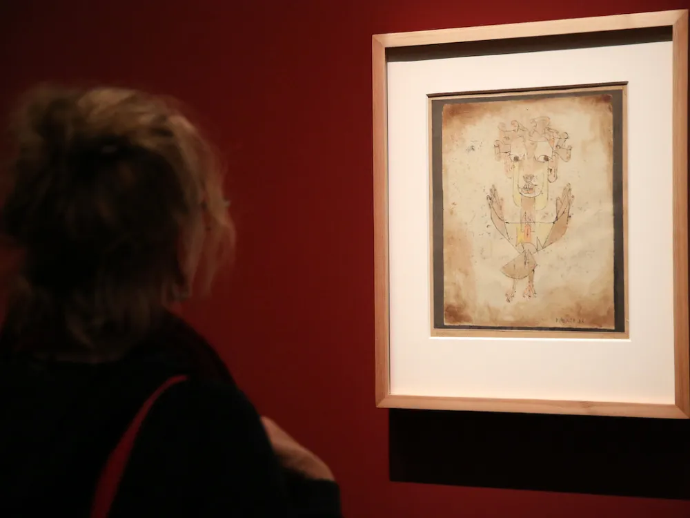 A woman looks at a paiting in a frame hung on a red wall.