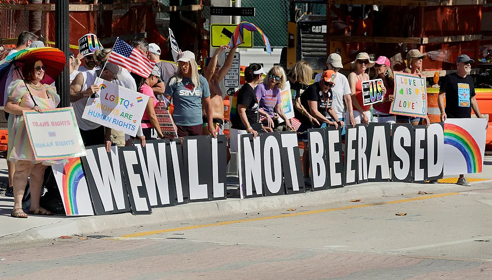 People holding signs stand on a sidewalk.