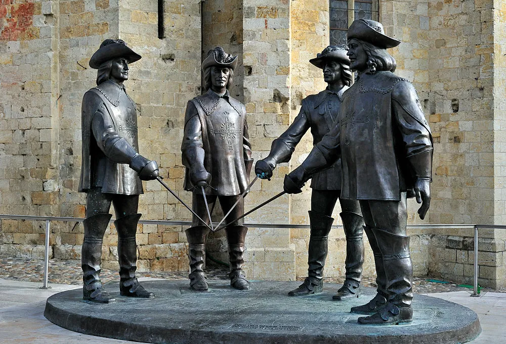 Bronze statue of four male figures standing in a circle in 16th century dress holding swords and pointing them towards the middle of their circle