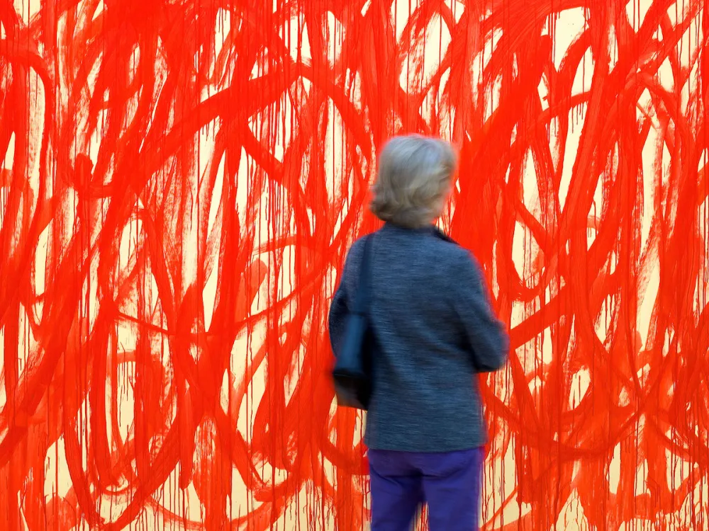 A woman seen from behind in front of a monumental painting filled with red swirls.