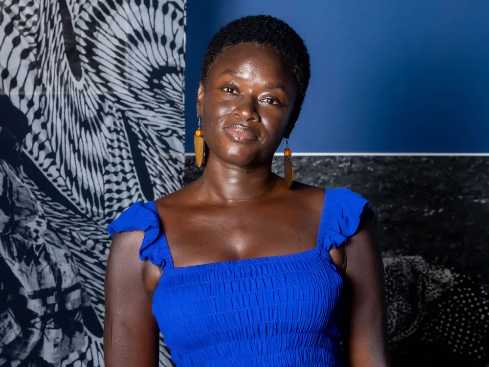 Portrait of Keisha Scarville in a bright blue dress standing in front of two abstract photographs.