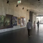 Visitors look at a photo-based, wall-hung installation on a grey concrete wall.