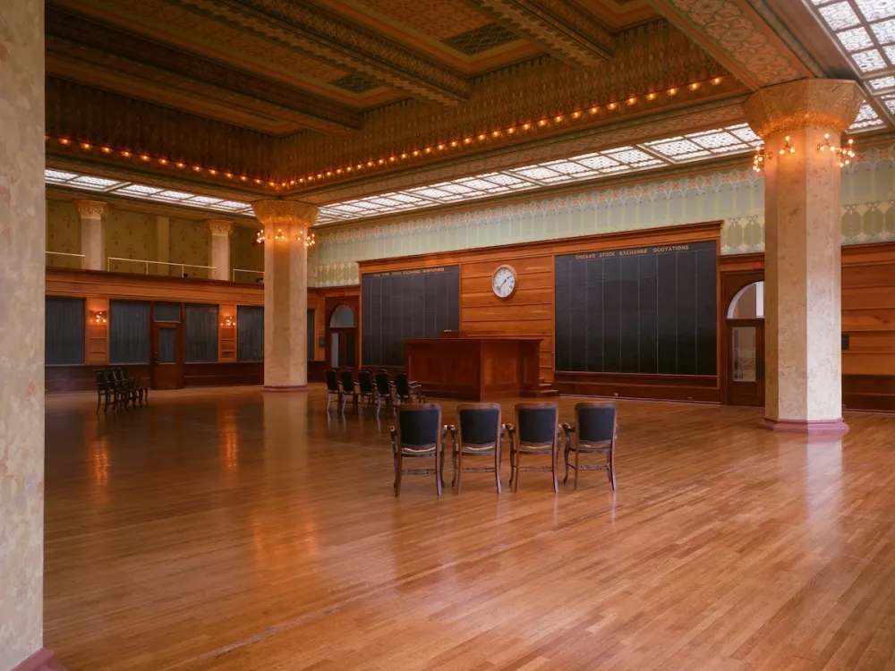 An empty room with two rows of chairs in it. Heavy columns with lights strung around them hold up an ornate ceiling.