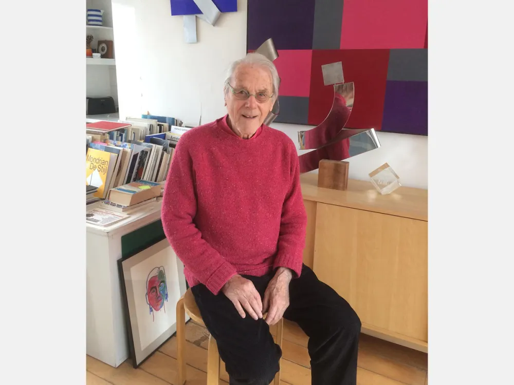 A man in a pink sweater in front of graphic designs.