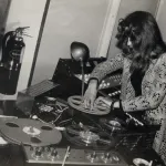 A woman handling spools of tape and electronic-music gear.