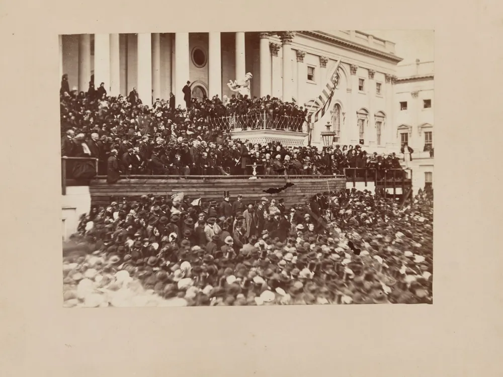 A vintage, sepia-toned photograph of a mass of people in front of the unfinished US Capitol.