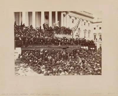 A vintage, sepia-toned photograph of a mass of people in front of the unfinished US Capitol.