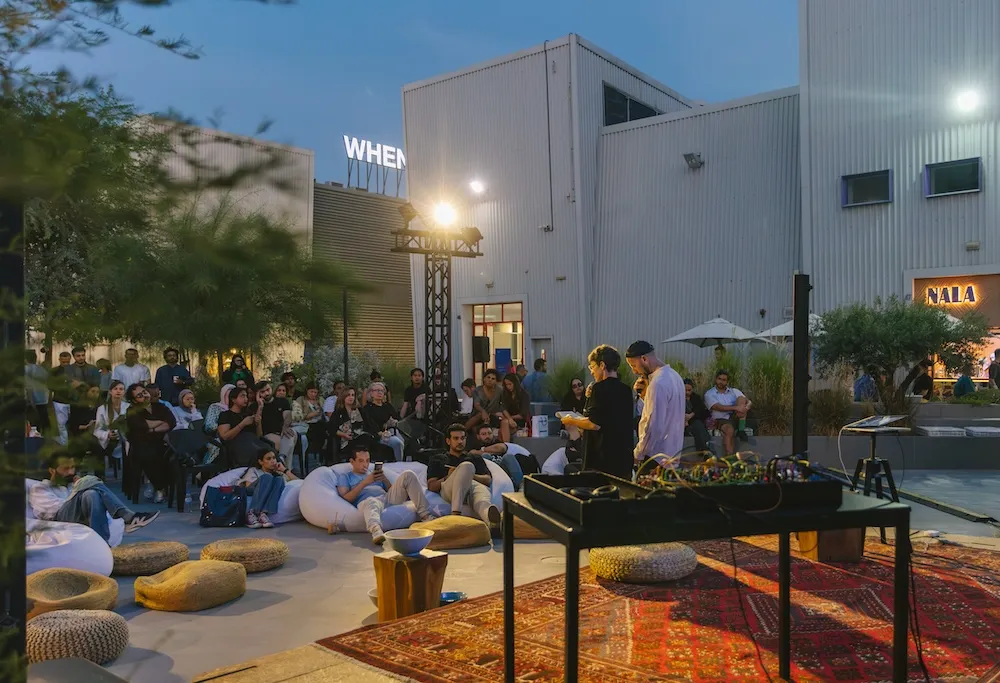 Two people read in front of an audience in the main square of Alserkal Avenue in Dubai.