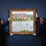 Two art handlers hold a brightly colored landscape painting by French Impressionist Claude Monet up against a dark-colored wall