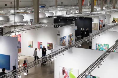 A photo shows rows of white-walled booths at the Expo Chicago art fair with artworks on the wall and visitors in the aisles