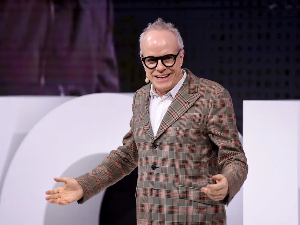 A man in a blazer with his arms spread.