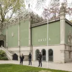 Three guards standing before a blocky green pavilion that has the word