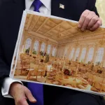 A man in a suit holding up a photograph of a ballroom.