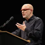 Portrait of Brian Eno speaking at a podium.