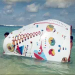 Two men hold up an unstretched canvas of an abstract painting in the water.
