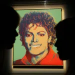 A painting of a smiling man with the silhouettes of two people in front of it.