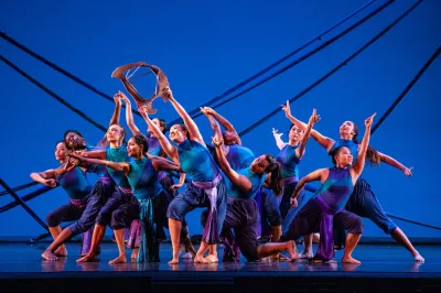 Performers dancing in a modern ensemble against a blue background. 