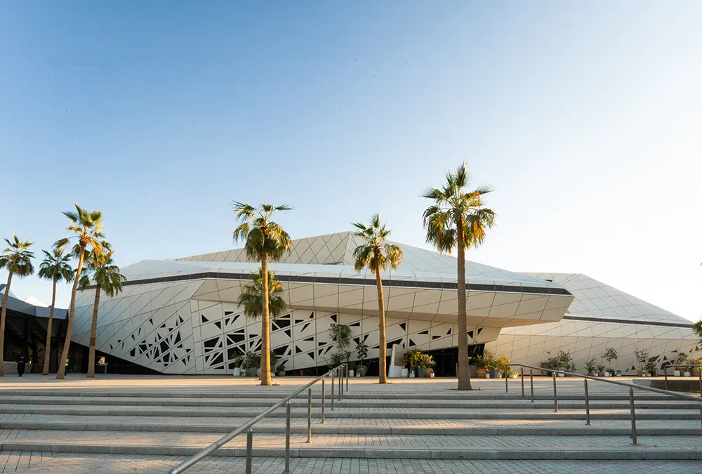 exterior view of an angular modern building with palm trees in front and a staircase in the foreground